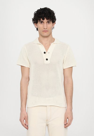 Polo shirt tricotat de culoare crem, cu mâneci scurte, având un guler și trei butoane negre. Model texturat cu țesătură deschisă.