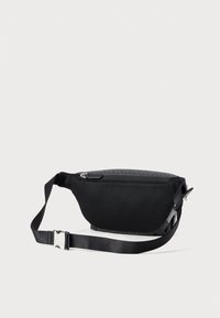 Borsa in rete nera con tasca con zip, strap regolabile e fibbia argentata su uno sfondo chiaro e semplice.