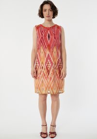 Robe sans manches en A avec un imprimé géométrique coloré dans des teintes de rouge et d'orange. Encolure ronde avec un accent de perles. Texture de tissu lisse.