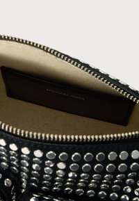 Schwarze Ledertasche mit silbernen Nieten, Reißverschluss und beigem Stoffinnenraum. Mit einem Etikett, das "Michael Kors" zeigt.