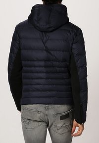 Marinblå puffjacka med huva, med quiltat mönster, svarta sidopaneler och dragkedjedetaljer. Texturerad tyg, slim fit.