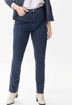 Dunkelblaue Jeans mit Slim-Fit, ausgestattet mit einem Knopfverschluss, Fronttaschen und einer glatten Denim-Oberfläche; getragen mit hellen Absätzen.