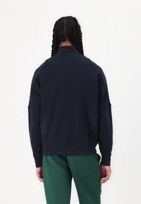 Marineblå sweatshirt med høy krage, raglanermer og ribbestrikkede mansjetter. Jevn tekstur, minimalt design, ingen synlige logoer eller mønstre.