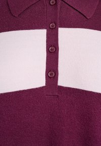 Camisa polo de punto con cuerpo en color burdeos y una franja horizontal en rosa claro que contrasta. Presenta un cuello y cuatro botones burdeos. Textura suave.