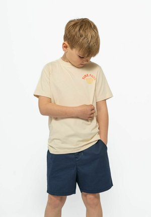 Beige Baumwoll-T-Shirt mit dem Text "TIME FLIES" und einer Muschelgrafik auf der Brust, kombiniert mit marineblauen Shorts. Schlicht, lockere Passform.