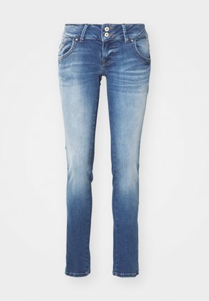 Úzke modré džínsy s vyblednutým priedzvukom. Obsahujú dve predné vrecká a zapínanie na gombík, s diskrétnym opotrebením pri spodnom leme.