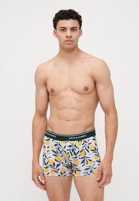 Boxers pour hommes en tissu bleu clair avec des motifs de citrons jaunes et une ceinture élastique vert foncé avec logo.