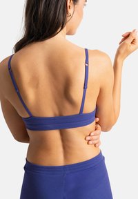 Bralette violet à coteaux avec des bretelles réglables. Tissu lisse avec une coupe ajustée, comprenant une large bande pour le soutien et un matériel minimal.