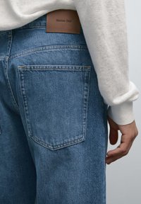 Jeans in denim blu con una vestibilità comoda, dotati di due tasche posteriori e un'etichetta in pelle marrone con "Massimo Dutti" sulla vita.