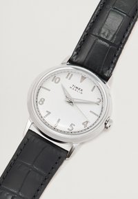 Relógio Timex Marlin prateado com caixa redonda, pulseira de couro com padrão de crocodilo preto e marcadores de horas numéricos em um mostrador prateado texturizado.