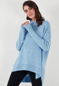 Gaiši zils, pārāk liels adīts džemperis ar ribotu apakšmalu un aprocēm, ar augstu-zemu dizainu. Mīksta tekstūra, brīvs piegriezums, garas piedurknes.