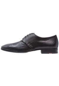 Chaussure habillée noire avec une tige texturée à motif quadrillé, bout arrondi et semelle plate. Fermeture à lacets avec un détail de marque discret sur le talon.