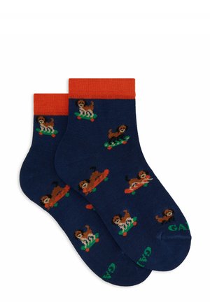 Marineblaue Socken mit orangefarbenen Bündchen, die ein wiederholtes Muster von bunten Hunden auf Skateboards zeigen. Text "GAP" in grün an der Sohle. Strickstruktur.