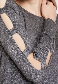 Metallic silver top featuring long sleeves with cut-out accents. The fabric has a textured, glittery appearance, enhancing its visual interest.