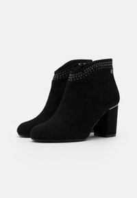 Botines de ante negro con puntera redondeada, decorados con tachuelas plateadas alrededor del cuello, y un tacón cuadrado y grueso.