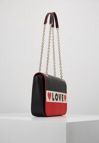 Černá a červená kožená kabelka obdélníkového tvaru, s řetízkem na rameno a předním panelem s výrazným nápisem "LOVE" a červenými srdíčky.