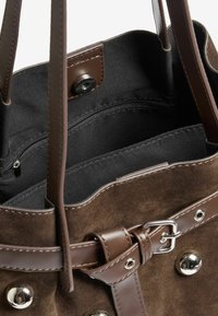 Barna velúr bevásárlótáska bőr kiegészítőkkel, belsejében cipzáras zsebbel és fém részletekkel. Puha tapintás és strukturált forma.