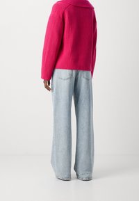 Jasnoróżowy sweter z prążkowanego dzianiny w połączeniu z jasnoniebieskimi spodniami o szerokich nogawkach. Sweter ma luźny krój i wyostrzony kołnierz.
