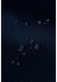 Ciemnoniebieska tkanina o teksturowanej powierzchni, na której widać kilka wyraźnych kropli wody, podkreślających jej wodoodporne właściwości.