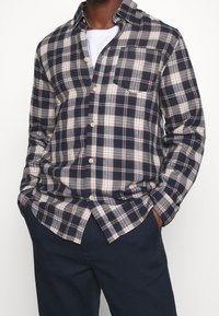 Koszula w niebiesko-beżową kratkę z długimi rękawami, z przodu zapinana na guziki, z kieszenią na piersi. Nosi się ją na białej koszulce, zestawioną z ciemnoniebieskimi spodniami.