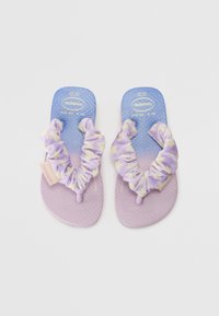 Violet šlepetės su tekstūruotais padukais, turinčios minkštą, tinklo spalvos audinio dirželį violetinėje ir geltonoje spalvose, bei mažą prekės ženklo etiketę šone.
