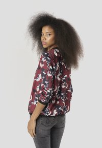 Bloemen bomberjack in bordeauxrood, met een mix van zwarte en witte patronen, lichtgewicht stof en geribbelde manchetten. Grijze spijkerbroek en getextureerd haar zichtbaar.