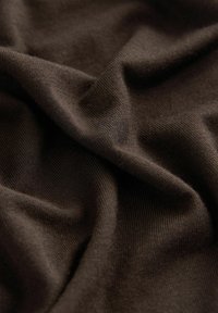 Tessuto lavorato a maglia marrone con una texture liscia, caratterizzato da fine rigature e una caduta morbida, con pieghe e increspature visibili.