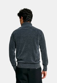 Pull collo alto grigio scuro, con tessuto texture, polsini e orlo a coste. Presenta un design semplice e informale senza motivi.