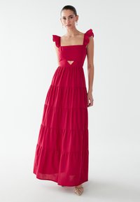 Vestido largo rojo con tirantes fruncidos, escote cuadrado y un detalle recortado. Cuenta con capas escalonadas y una silueta fluida.