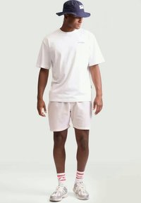 Witte katoenen T-shirt, lichte shorts, gecombineerd met een marineblauwe bucket hat. Accented met rood-witte gestreepte sokken en zilveren sneakers.