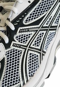 Scarpa da corsa bianca e nera in tessuto a rete con lacci, caratterizzata da un distintivo logo a motivo bianco e nero sul lato.