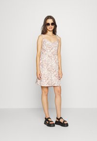 Vestido leve, sem mangas, com um padrão de paisley em pêssego e branco, formato em A e cintura ajustada. Acompanhado de sandálias plataformas pretas chunky.