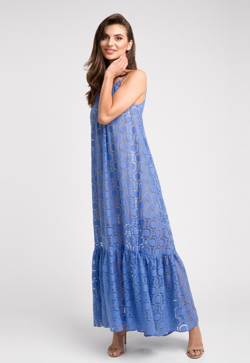 Maxi sukienka w jasnoniebieskim kolorze, z przezroczystą nakładką w okrągłe wzory, warstwowym dołem i ramiączkami na spaghetti. Teksturowany materiał podkreśla detale.