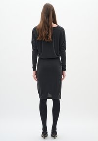 Crna majica dugih rukava opuštenog kroja, uparen s crnom olovkom suknjom do koljena. Glatka tekstura, jednolična boja i minimalistički dizajn.
