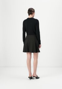 Čierny top s dlhým rukávom skombinovaný s tmavozelenou rozšírenou sukňou. Model má na sebe čierne slip-on topánky. Minimalistický dizajn, hladké textúry.