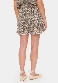 Leopardmönstrade shorts med scallopkant och elastisk midja, i kombination med beiga, platta snörskor i vävd textur.