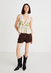 Floral-embroidered cream sleeveless top with lace trim, paired with brown suede shorts and black cowboy boots.