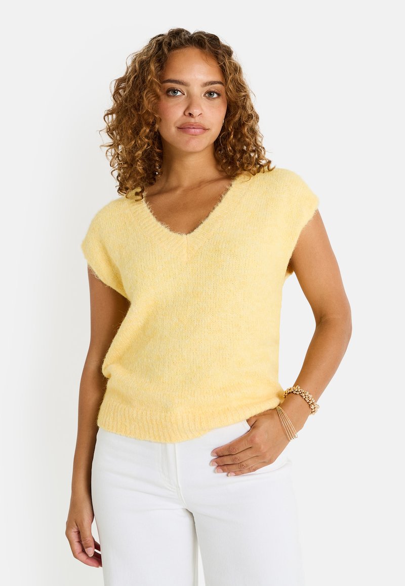 Suéter de punto amarillo de mangas cortas con escote en V, que presenta una textura suave y un dobladillo acanalado. Combinado con pantalones blancos, mostrando un ajuste relajado.