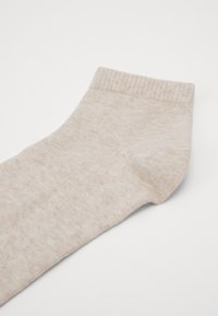 Calzino in cotone a coste beige con una texture morbida, caratterizzato da leggere variazioni di tonalità e una piccola pettinatura nella parte superiore.