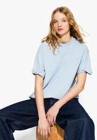 T-shirt in cotone azzurro chiaro con maniche corte arrotolate, scollatura rotonda e vestibilità rilassata, abbinato a jeans a gamba larga in denim scuro.
