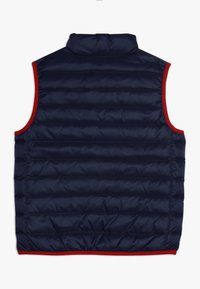 Chaleco acolchado azul marino con un alto cuello, con ribetes acentuados en rojo y textura de acolchado horizontal. Sin mangas, con dobladillo elástico.
