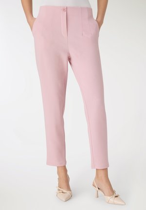 Pantaloni rosa chiaro su misura con fronte piatto, tasche laterali e vestibilità slim, abbinati a scarpe beige con tacco e un dettaglio a fiocco.