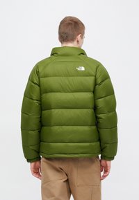 Zaļā pūkainā jaka ar kvadrātveida šuvumiem, ribotām aprocēm un augstu apkakli. Augšējā muguras daļā ir neliels balts logotips.