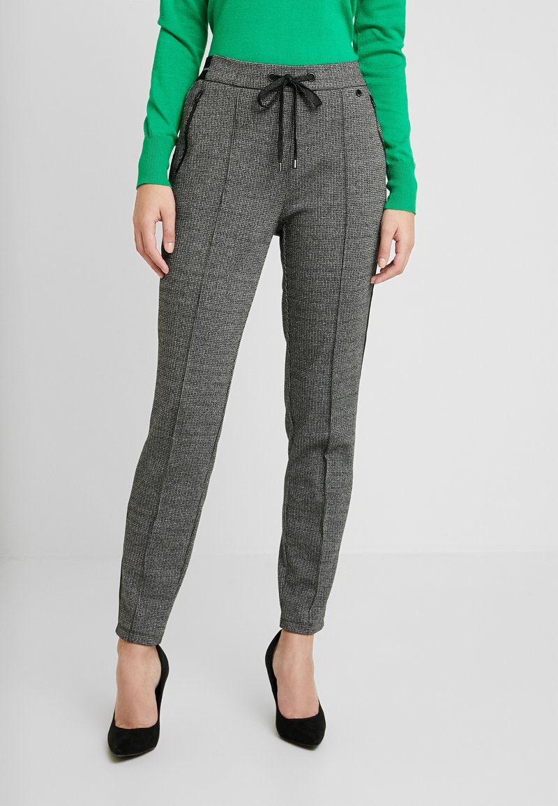 Pantalons gris à carreaux avec une taille à cordon, poches latérales et coupe slim. Associés avec des talons noirs et une chemise à manches longues verte.
