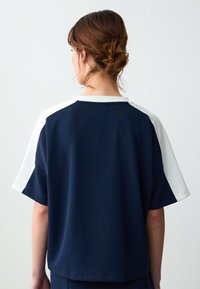 Donkerblauwe T-shirt met korte mouwen, witte schouderaccenten en een ronde halslijn. Glad materiaal en een ontspannen pasvorm, ontworpen voor comfort.