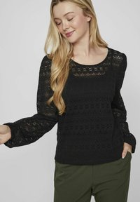 Mustmust särg pikade, puhvseintega varrukatega ja ümarate kraega; consts täiustatud kihilise mustriga. Kombineeritud roheliste pükstega.