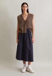 Brown short-sleeve knitted vest with button detail, paired with a dark navy midi skirt and white sneakers. Simple, textured, and layered outfit.