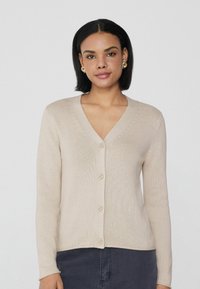Cárdigan beige hecho de tejido de punto, con cuello en V, seis botones y mangas largas. Textura suave con un sutil detalle de canalé.