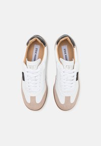 Balti sportbačiai su béžiniais zomšos akcentais, turintys apvalų nosį, raištelių dizainą ir juodą kulno juostą, paženklintą "STEVE MADDEN".