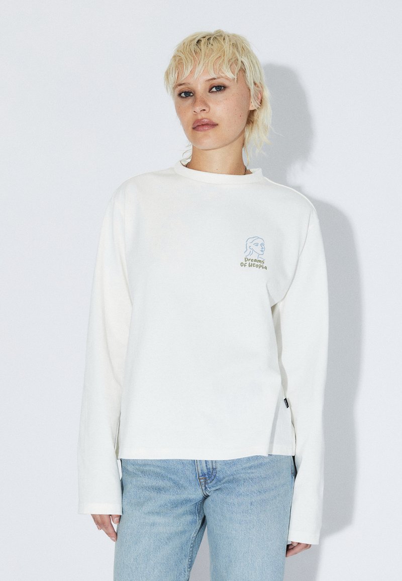 Sweat-shirt blanc à manches longues en tissu de coton doux, avec un motif graphique bleu sur la poitrine et des fentes latérales à l'ourlet.
